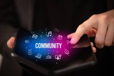 İş adamı, üzerinde COMUNITY yazıtları ve sosyal medya kavramı olan katlanabilir bir akıllı telefon tutuyor.
