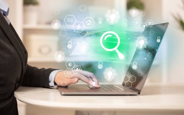 Eller, büyüteç simgeleri ve modern teknoloji konseptiyle dizüstü bilgisayarda çalışıyor.