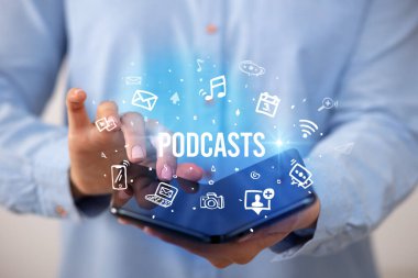 Podcast yazıları ve sosyal medya konsepti olan katlanabilir bir akıllı telefon tutan bir iş adamı