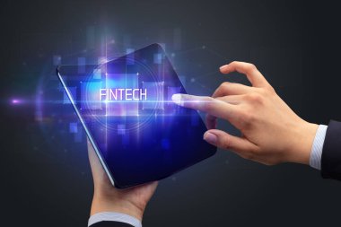 FINTECH yazıtları ve yeni teknoloji konsepti olan katlanabilir bir akıllı telefon tutan bir iş adamı