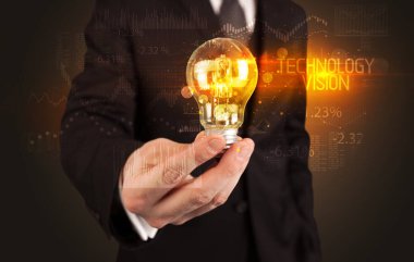 TEKNOLOJİ VISION yazıtları ve iş teknolojisi kavramına sahip bir iş adamı elinde ampul tutuyor