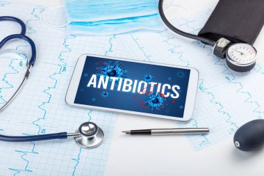 Beyaz yüzeyde ANTIBIOTICS yazıtları, salgın konsepti olan tablet pc ve doktor araçları