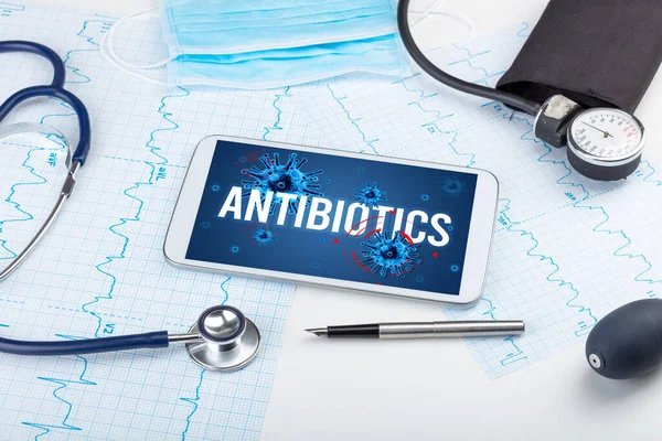 Beyaz yüzeyde ANTIBIOTICS yazıtları, salgın konsepti olan tablet pc ve doktor araçları