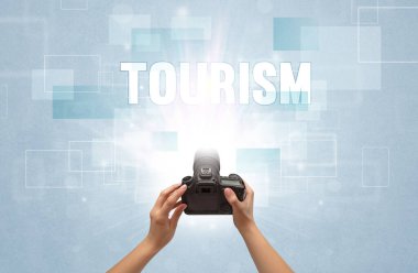 TOURISM yazıtları ve seyahat konseptiyle el ele tutuşan dijital kameranın yakın çekimi