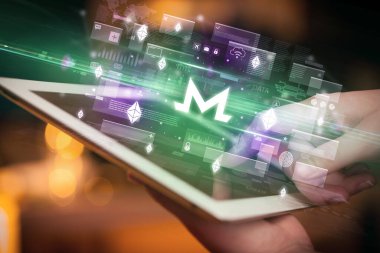 İçinden monero simgeleri çıkan tablet kullanan bir elin yakın çekimi, dijital para birimi kavramı