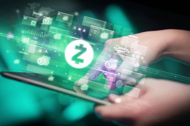 İçinden zcash simgeleri çıkan tablet kullanan bir elin yakın çekimi, dijital para birimi kavramı