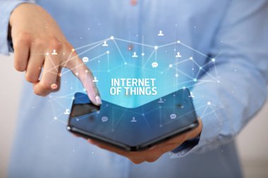 İş adamı elinde, üzerinde yeni teknoloji kavramı ve yazıtların olduğu katlanabilir bir akıllı telefon tutuyor.