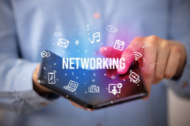 İş adamı elinde NETworking yazıtlı, sosyal medya kavramlı katlanabilir bir akıllı telefon tutuyor.