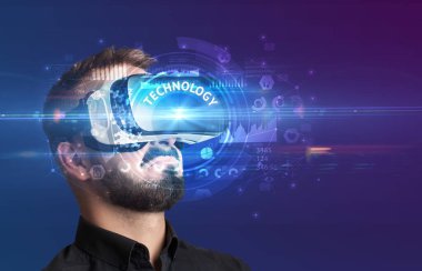 TECHNOLOGY yazıtları ve yenilikçi teknoloji konseptiyle Sanal Gerçeklik gözlüklerine bakan iş adamı