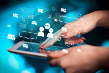 Tablet kullanan ve içinden ikonlar çıkan bir elin yakın plan resmi, sosyal medya kavramı