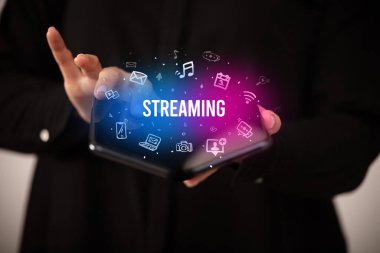 İş adamı elinde katlanabilir bir akıllı telefon tutuyor. Üzerinde STREAMING yazıtları ve sosyal medya kavramı var.