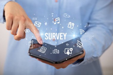 İş adamı elinde katlanabilir bir akıllı telefon tutuyor. Üzerinde SURVEY yazıları, sosyal medya kavramı var.