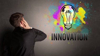 İş adamı desenli beton duvara INNOVATION yazısıyla renkli ampul çiziyor, yeni iş fikri kavramı