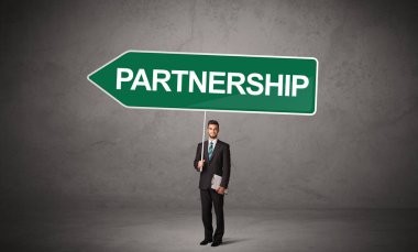 Genç iş adamı, üzerinde PARTNERGeIP yazıları ve yeni iş yönü konsepti olan günlük bekleme yolu tabelasında.