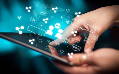 Tablet kullanan ve içinden ikonlar çıkan bir elin yakın plan resmi, sosyal medya kavramı