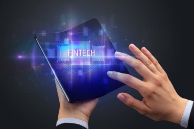 FINTECH yazıtları ve yeni teknoloji konsepti olan katlanabilir bir akıllı telefon tutan bir iş adamı