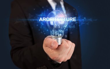 ARCHITECTURE yazıtlı, yenilikçi teknoloji kavramına sahip bir iş adamı elinde ampul tutuyor