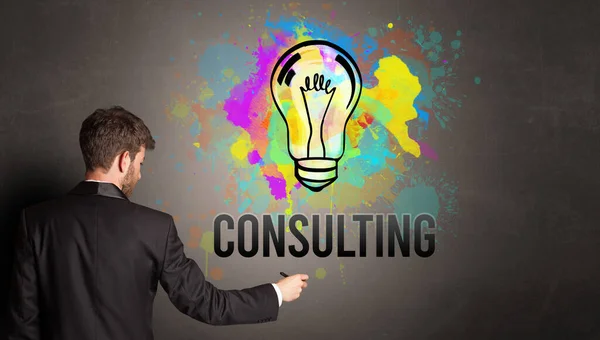 Businessman Drawing Colorful Light Bulb Consulting Inscription Textured Concrete Wall — 图库照片