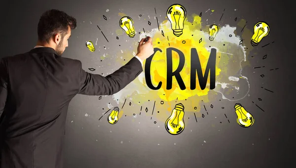 businessman drawing colorful light bulb with CRM abbreviation, new technology idea concept