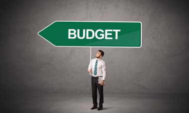 Bütçe yazıtları ve yeni iş yönü konseptiyle günlük bekleme yolu tabelasında genç iş adamı