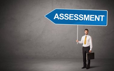 Genç iş adamı, günlük bekleme yolu tabelasında ASSESSMENT yazısıyla, yeni iş yönü konseptiyle