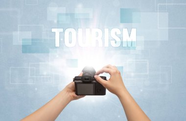 TOURISM yazıtları ve seyahat konseptiyle el ele tutuşan dijital kameranın yakın çekimi