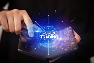 İş adamı elinde FOREX TRADING yazıtları ve yeni iş konseptiyle katlanabilir bir akıllı telefon tutuyor.