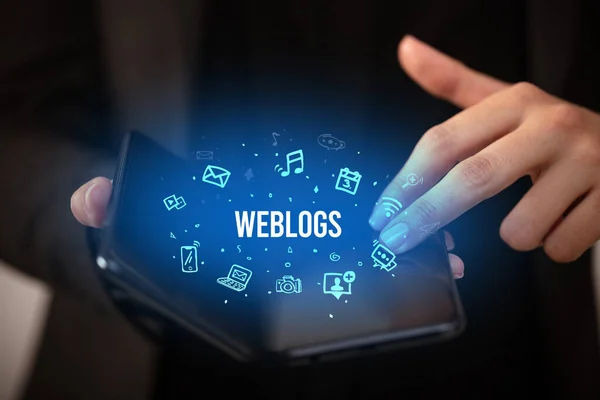 ビジネスマンは Weblogsの碑文 ソーシャルメディアの概念を持つ折り畳み式のスマートフォンを保持 — ストック写真