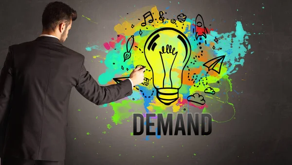 Businessman Drawing Colorful Light Bulb Demand Inscription Textured Concrete Wall — Stock Photo, Image