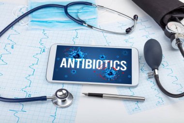 Beyaz yüzeyde ANTIBIOTICS yazıtları, salgın konsepti olan tablet pc ve doktor araçları