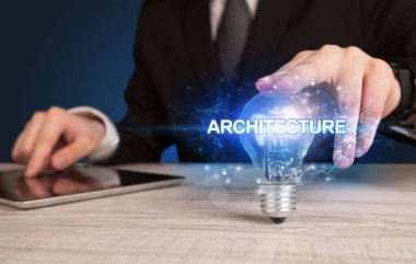 ARCHITECTURE yazıtlı, yenilikçi teknoloji kavramına sahip bir iş adamı elinde ampul tutuyor