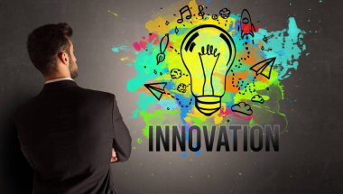 İş adamı desenli beton duvara INNOVATION yazısıyla renkli ampul çiziyor, yeni iş fikri kavramı