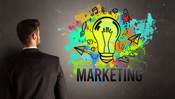 テクスチャコンクリート壁にマーケティングの碑文とカラフルな電球を描くビジネスマン 新しいビジネスアイデアのコンセプト — ストック写真