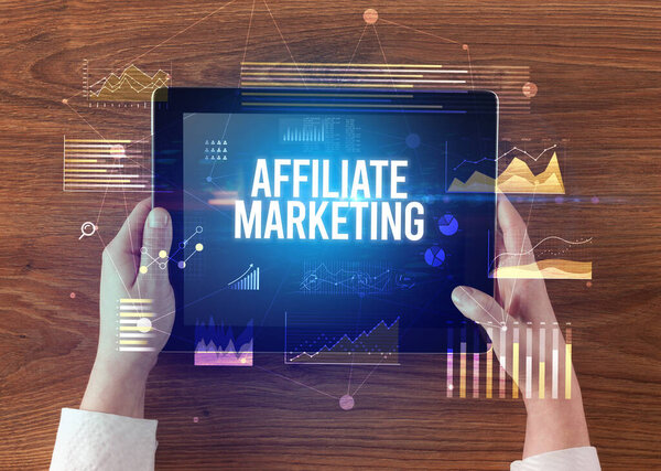 Close-up of hands holding tablet with AFFILIATE MARKETING inscription, modern business concept
