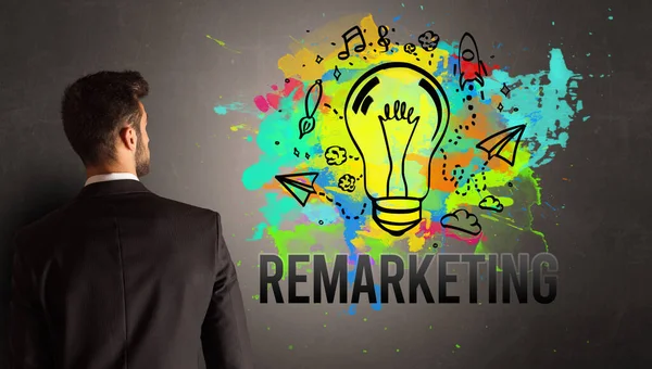 テクスチャコンクリート壁にRemarketing碑文とカラフルな電球を描くビジネスマン 新しいビジネスアイデアのコンセプト — ストック写真