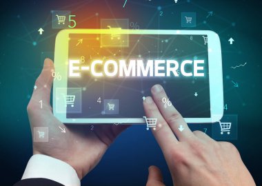 E-COMERCE yazıtları ve online alışveriş konseptiyle el ele tutuşan tabletin yakın çekimi