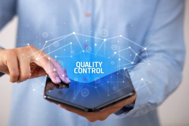 İş adamı elinde katlanabilir bir akıllı telefon tutuyor. KALİTLİK KONTROL yazıtları, yeni teknoloji kavramı