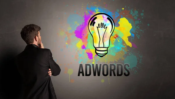 商人画五彩缤纷的灯泡 上面印有Adwords字样的纹理混凝土墙 新的商业理念 — 图库照片