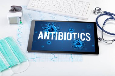 Beyaz yüzeyde ANTIBIOTICS yazıtları, salgın konsepti olan tablet pc ve doktor araçları