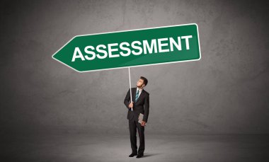 Genç iş adamı, günlük bekleme yolu tabelasında ASSESSMENT yazısıyla, yeni iş yönü konseptiyle