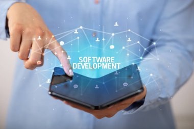 İş adamı elinde SOFTWARE DEVELOPMENT yazıtlı katlanabilir bir akıllı telefon tutuyor, yeni teknoloji konsepti