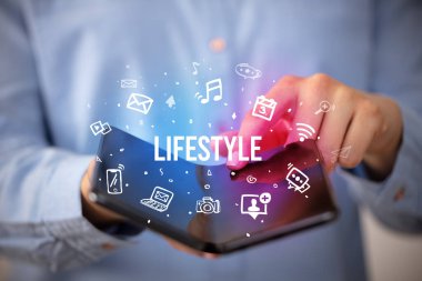 İş adamı, üzerinde LIFESTYLE yazıları ve sosyal medya kavramı olan katlanabilir bir akıllı telefon tutuyor.