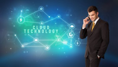 Cloud Technology yazıtları ve modern teknoloji konseptiyle bulut servisi simgelerinin önündeki iş adamı