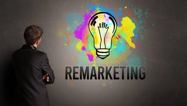 テクスチャコンクリート壁にRemarketing碑文とカラフルな電球を描くビジネスマン 新しいビジネスアイデアのコンセプト — ストック写真