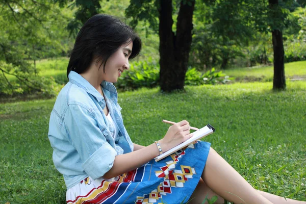 Красива молода жінка пише на відкритому повітрі в парку Стокове Фото