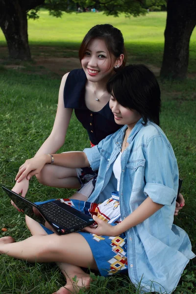 Two beautiful girl on a laptop computer outdoors. Lay on the gre — Stock Photo, Image