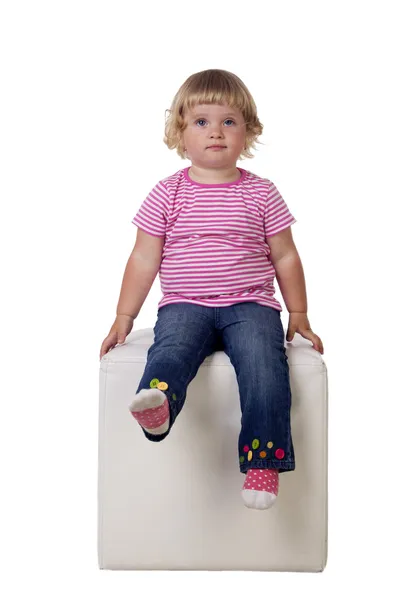 Malá holčička se sedí na bílé krychli, izolovaných na bílém pozadí — Stock fotografie