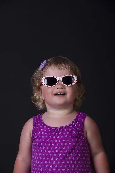 Petite fille avec des lunettes de soleil posant sur un fond noir — Photo