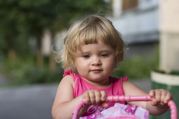 Cute baby girl with toy stroller outdoor — Stock Photo, Image