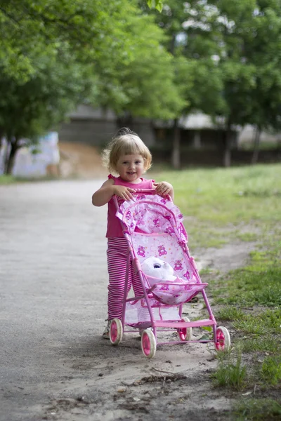 Cute dziewczynka z wózek zabawka zewnątrz — Zdjęcie stockowe